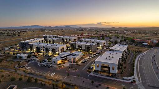 A sunset view of a modern building complex with a parking lot in front.