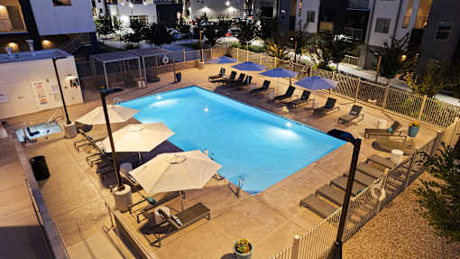 A pool surrounded by chairs and umbrellas at night.