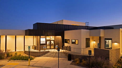 A modern building with a dark facade and a lit entrance.