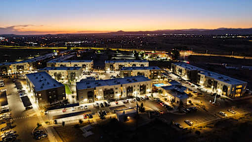 A large building complex is lit up at night with cars parked in front.