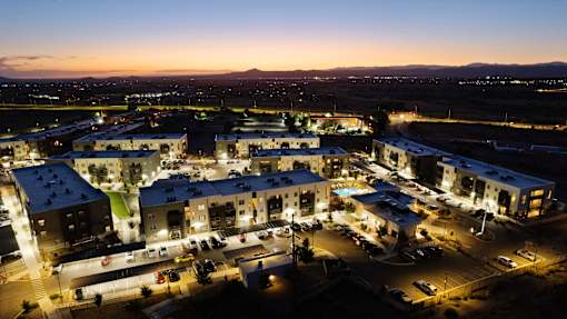 A large building complex is lit up at night with cars parked in the lot.