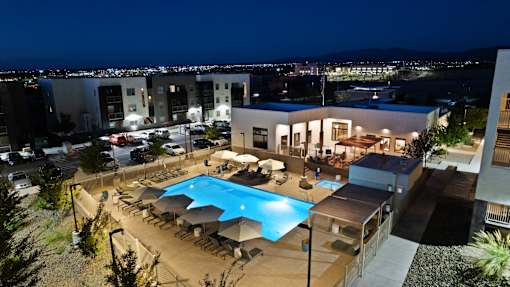 A swimming pool surrounded by lounge chairs and umbrellas is lit up at night.
