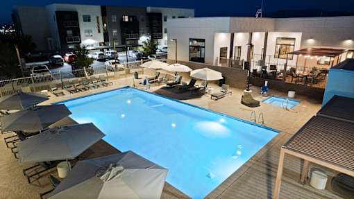A swimming pool surrounded by lounge chairs and umbrellas at night.