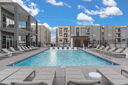 A swimming pool surrounded by lounge chairs in front of apartment buildings.