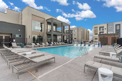 A pool area with sun loungers and a building in the background.
