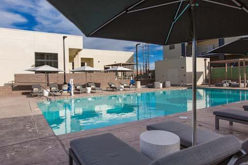 A pool with a black umbrella and grey couches.