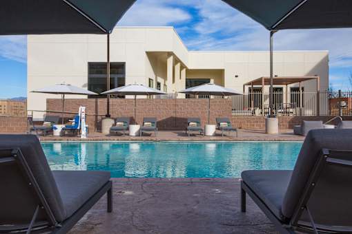 A pool area with lounge chairs and umbrellas in front of a modern building.