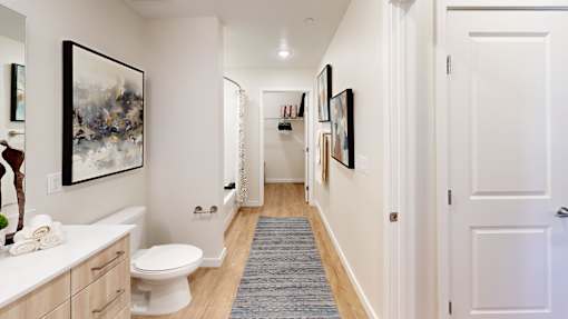 A hallway with a toilet, sink, and pictures on the wall.
