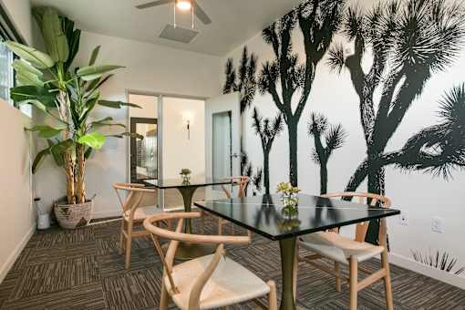 A dining room with a table and chairs and a tree mural on the wall.