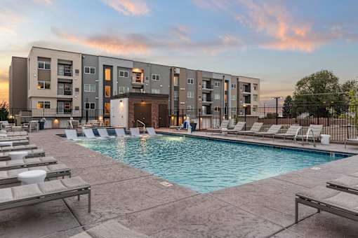 A swimming pool surrounded by lounge chairs in front of apartment buildings.