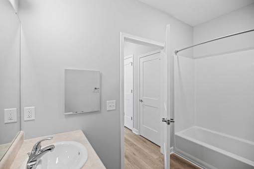 A white bathroom with a sink, mirror, and bathtub.