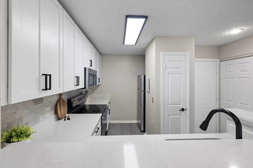 A kitchen with white cabinets and a black faucet.