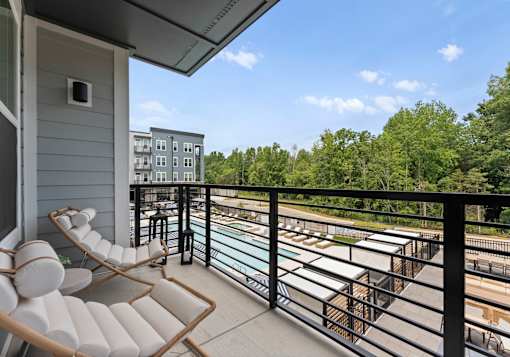 A balcony with a chair and table overlooking a pool and trees.