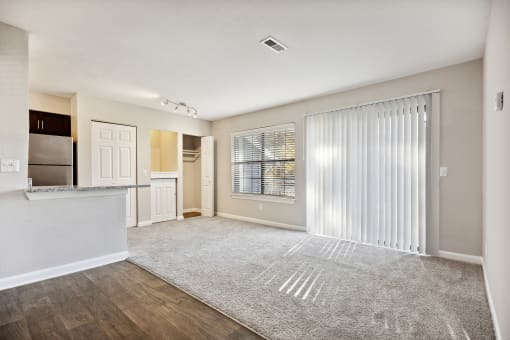 the living room and kitchen of an apartment with a large window and sliding glass doors