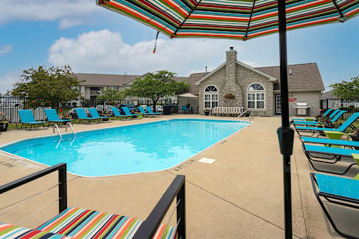 A pool with a striped umbrella and chairs.