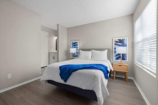 A bedroom with a bed, nightstand, and a window with blinds.