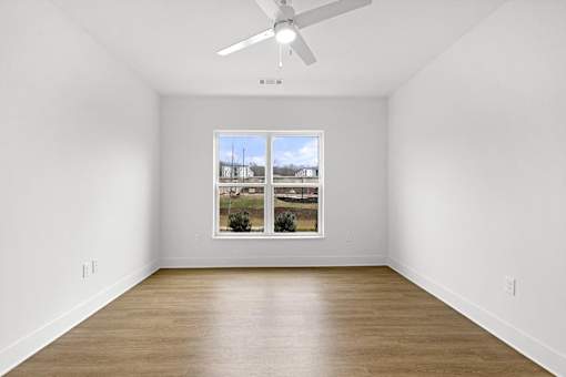 A room with a ceiling fan and a window showing a view of a house.
