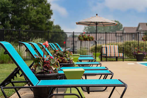 A row of blue and green lawn chairs are arranged in a row by a pool.
