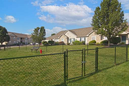 A black fence surrounds a green field with houses in the background.