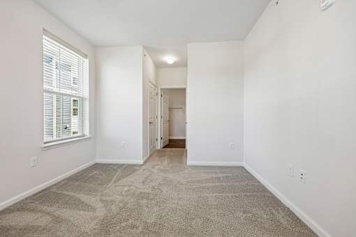 A room with a carpeted floor and a window with blinds.