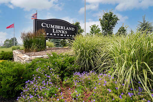 A sign for Cumberland Links Apartments is surrounded by greenery and flowers.
