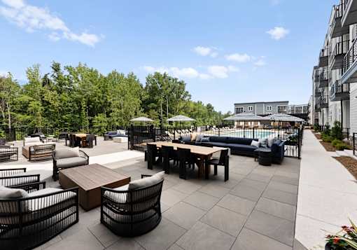 A patio with black chairs and tables is surrounded by trees.