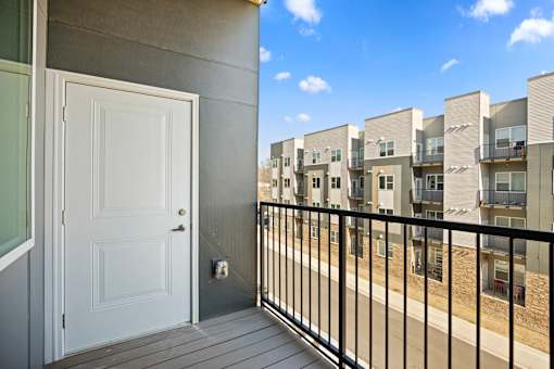 A white door is on the left of a balcony with a black railing.
