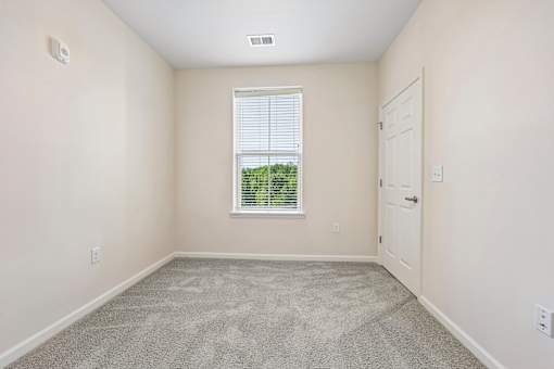 A room with a carpeted floor, a window with blinds, and a door.