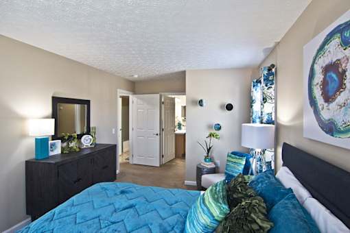 A bedroom with a blue bedspread and a painting on the wall.