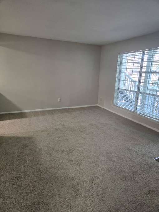 A room with a carpeted floor and a window with blinds.