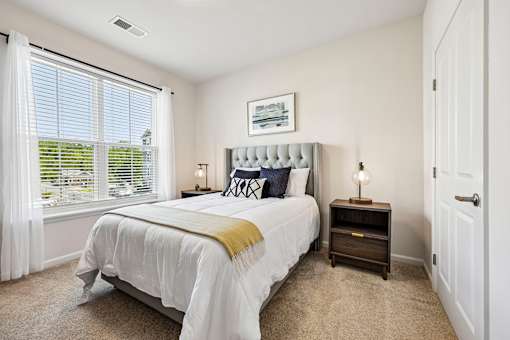 A bedroom with a large bed and a window with white curtains.