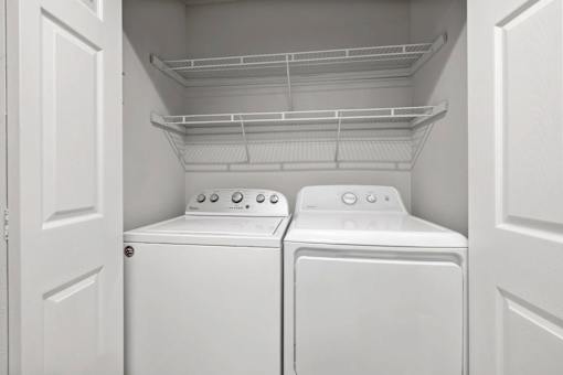 Two white washing machines in a white-walled laundry room.