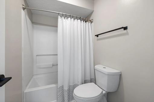 A white toilet with a white shower curtain in a bathroom.