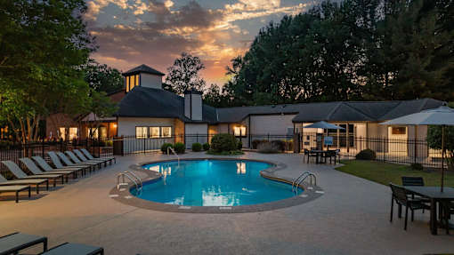 A pool surrounded by lounge chairs and umbrellas with a house in the background.