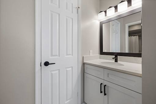 A white bathroom with a door, sink, and mirror.