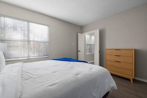 A bedroom with a white bed and a wooden dresser.