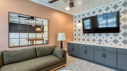 A living room with a grey sofa, a large mirror, and a television mounted on the wall.