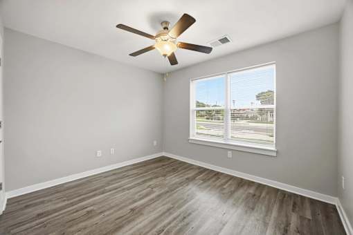 A room with a ceiling fan and a window overlooking a parking lot.