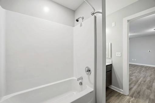A white bathroom with a tub and a doorway leading to another room.