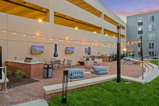 a patio with tables and chairs at a building with string lightsat Metropolis Apartments, Glen Allen, 23060