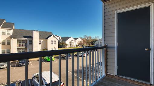 A balcony with a black door and a view of a parking lot with cars.
