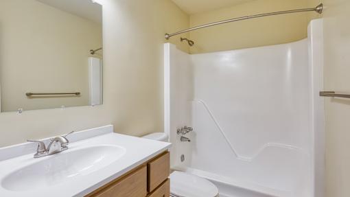 A white sink with a wooden counter top and a white bathtub with a shower curtain.