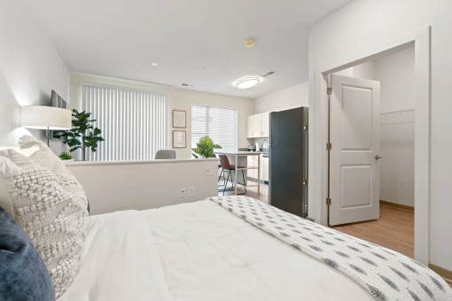 a bedroom with a white bed and a kitchen in the backgroundat Metropolis Apartments, Glen Allen, VA