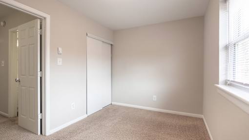 A room with a carpeted floor and a window with blinds.