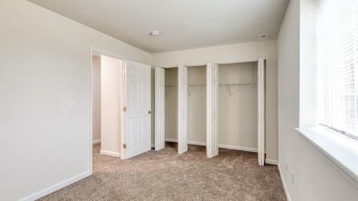 an empty bedroom with closet doors and a window