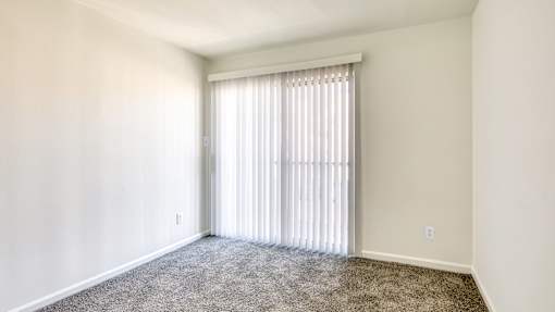 A room with a carpeted floor and a window with blinds.