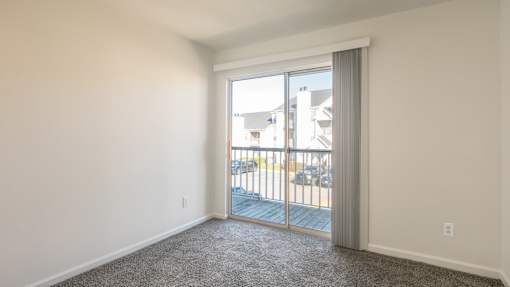 A room with a carpeted floor and a sliding glass door leading to a balcony.
