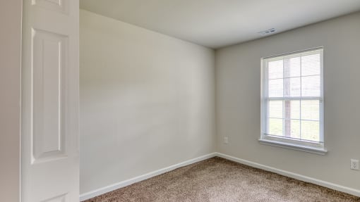 an empty bedroom with white walls and a window