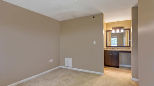 A room with beige walls and carpeting, a window with a view of trees, and a cabinet with a countertop.