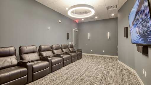 A row of brown leather recliner chairs are lined up in a room with a large screen on the wall.
